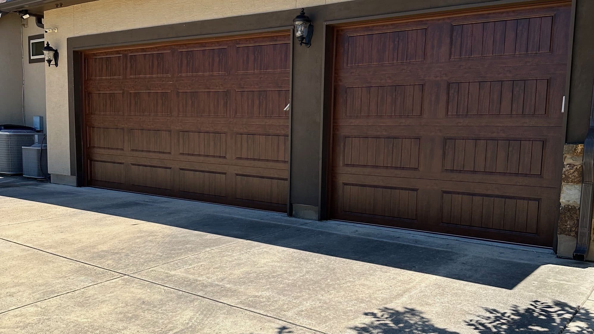 Two walnut carriage-style garage doors on a tan stucco home installed by SanTex Garage Doors