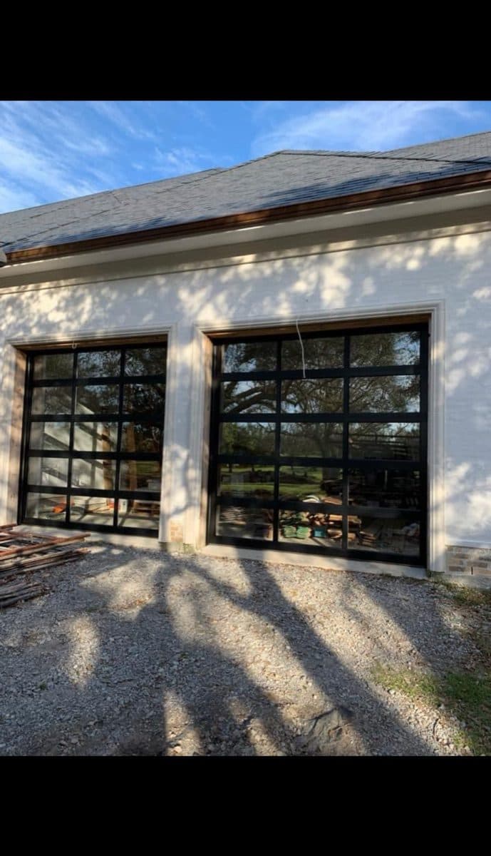 Two black full-view glass garage doors in white painted brick