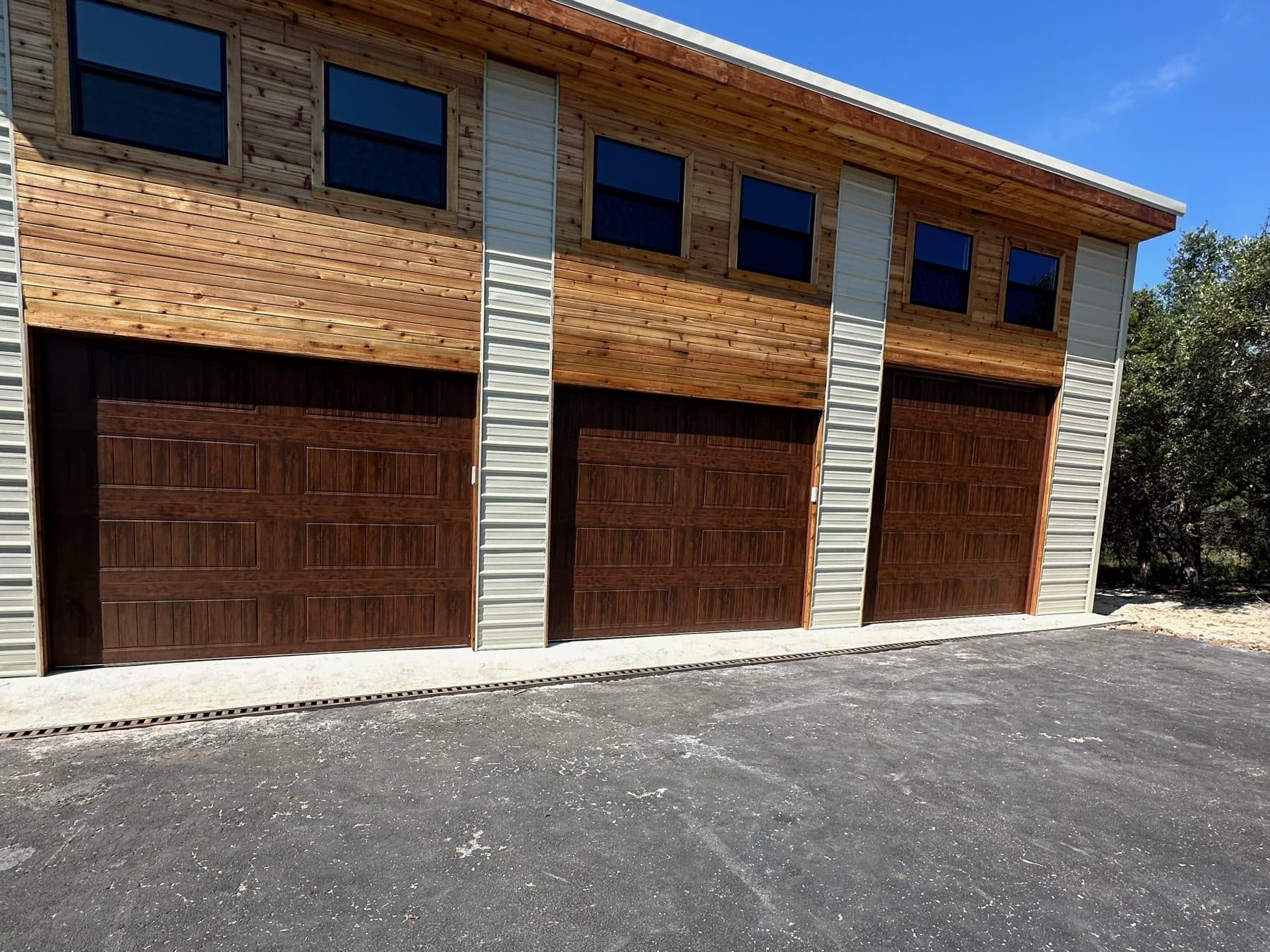 Three walnut garage doors on a cedar and metal shop building